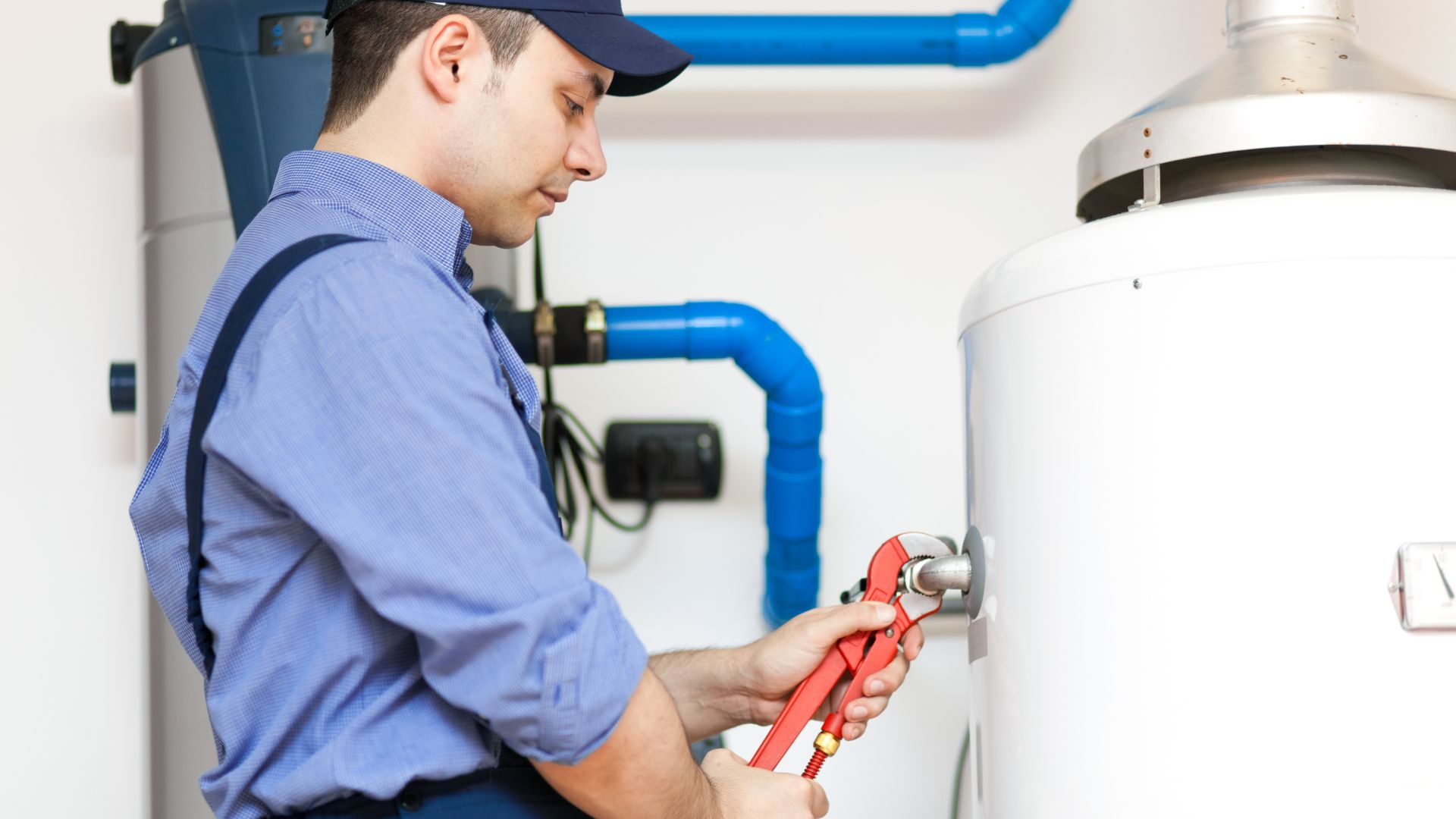 Technician using red pliers to repair water heater with blue pipes