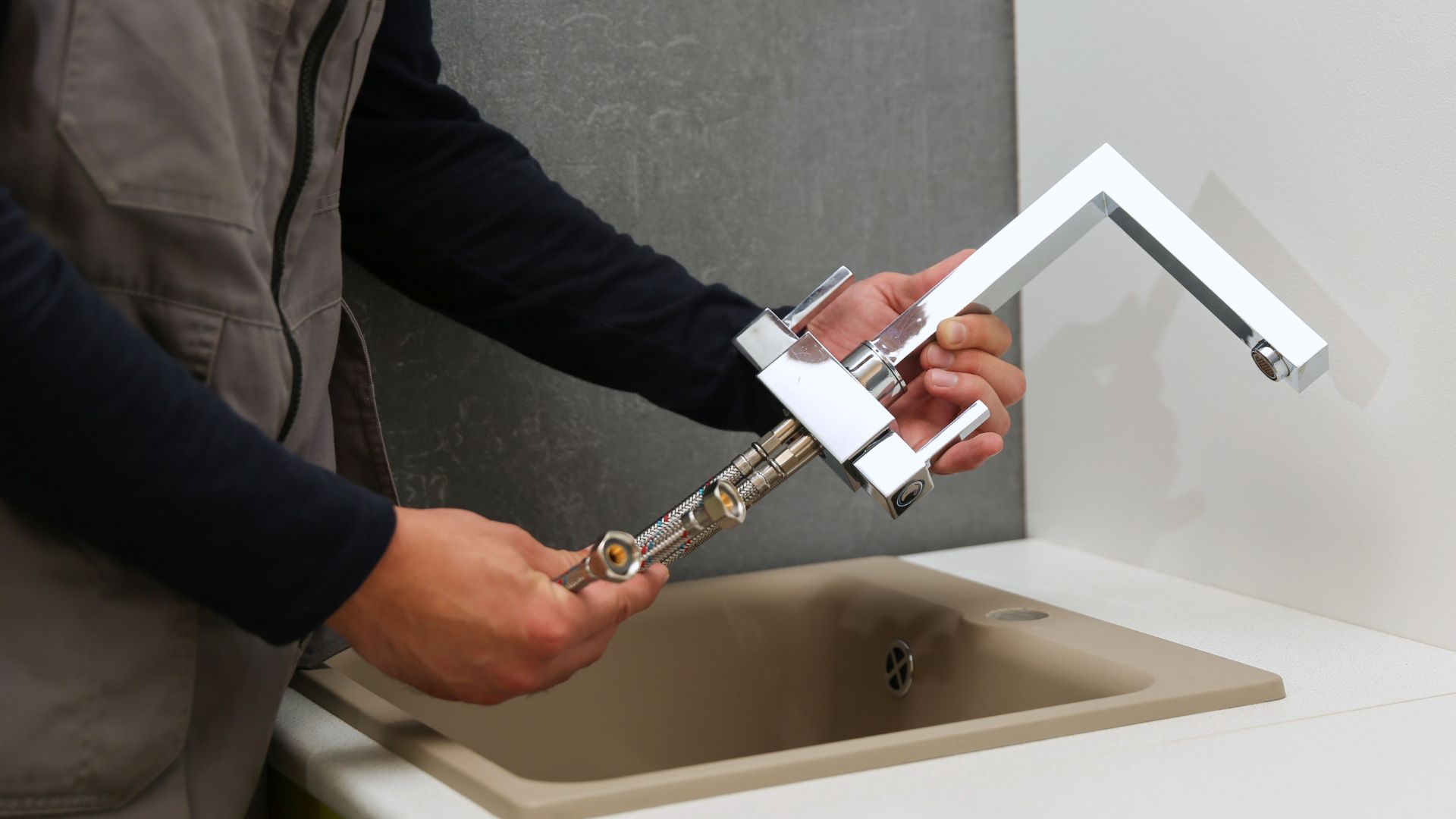 Hands installing a modern chrome bathroom faucet on a beige sink