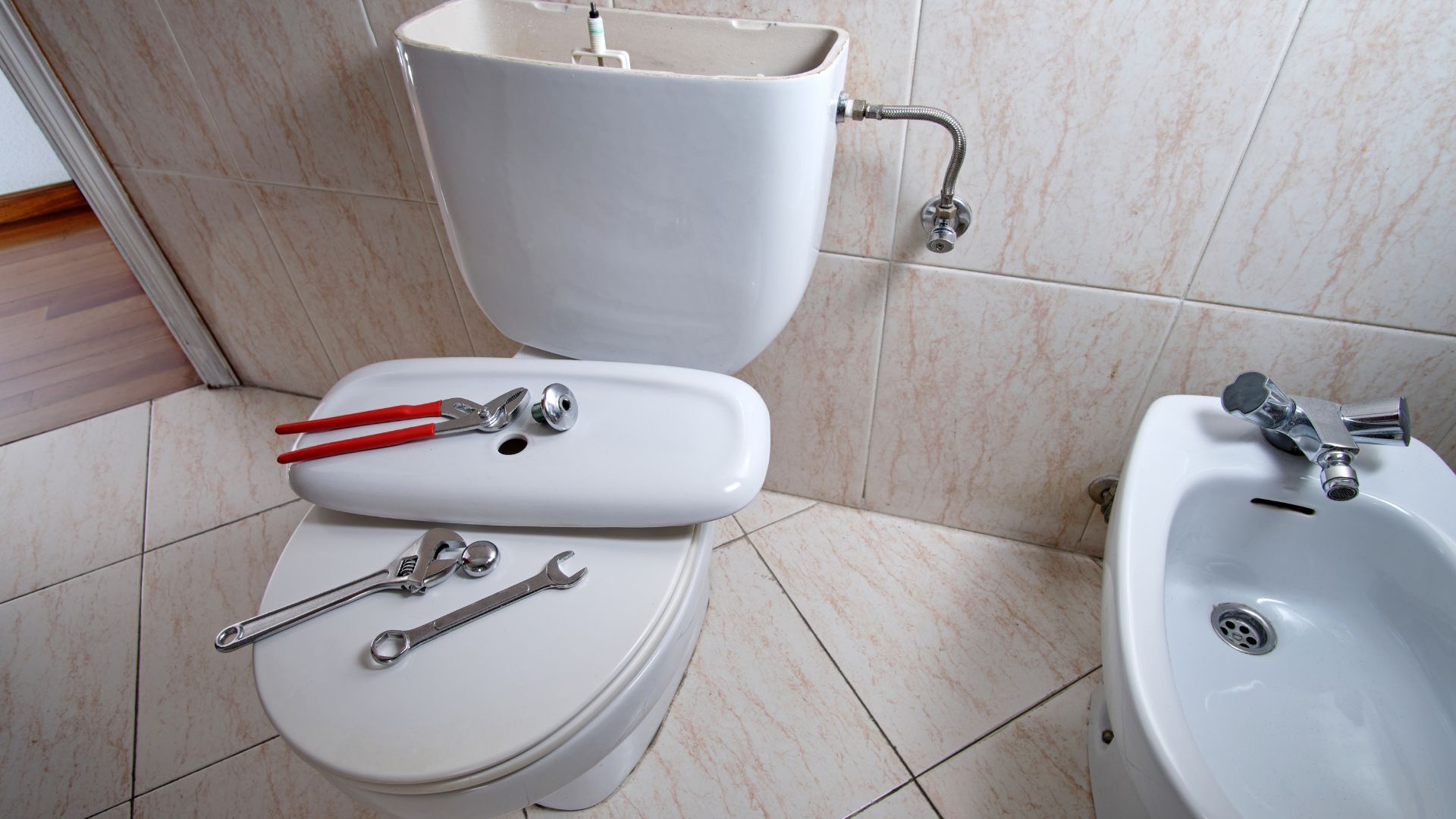 Plumbing tools on toilet in tiled bathroom with sink