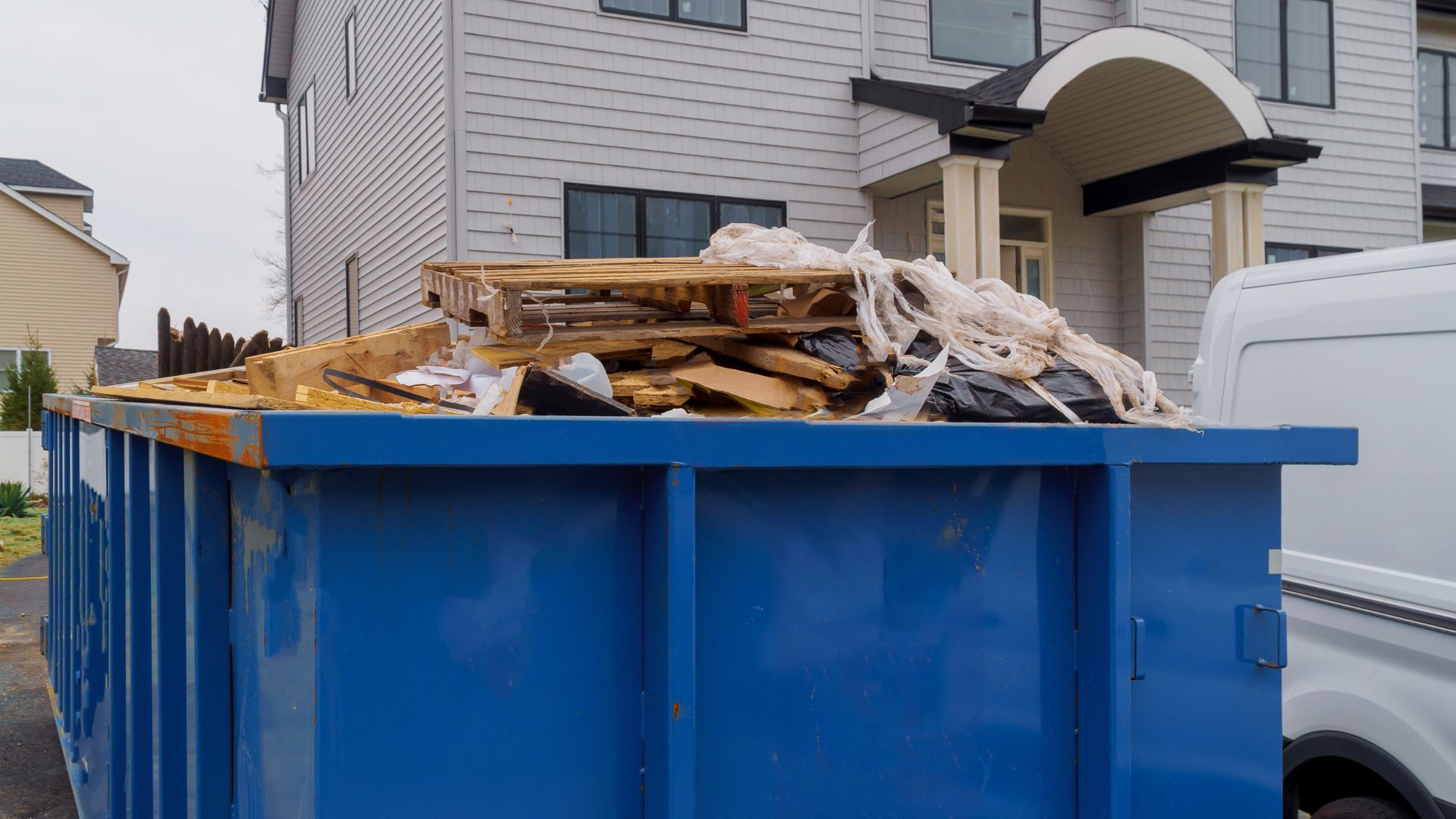 Blue dumpster filled with construction debris near residential building
