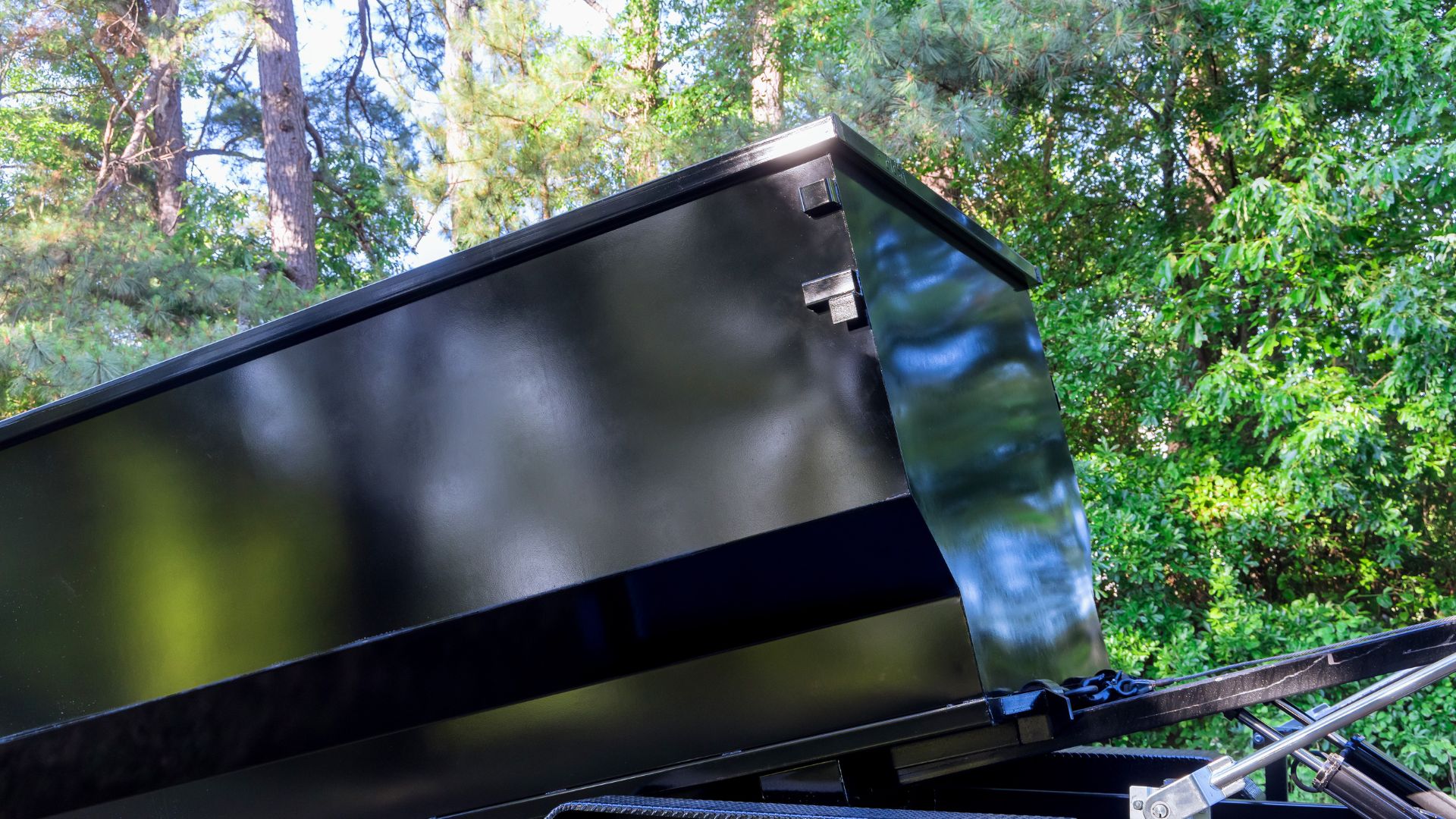 Black trailer or dumpster with raised lid in forest setting