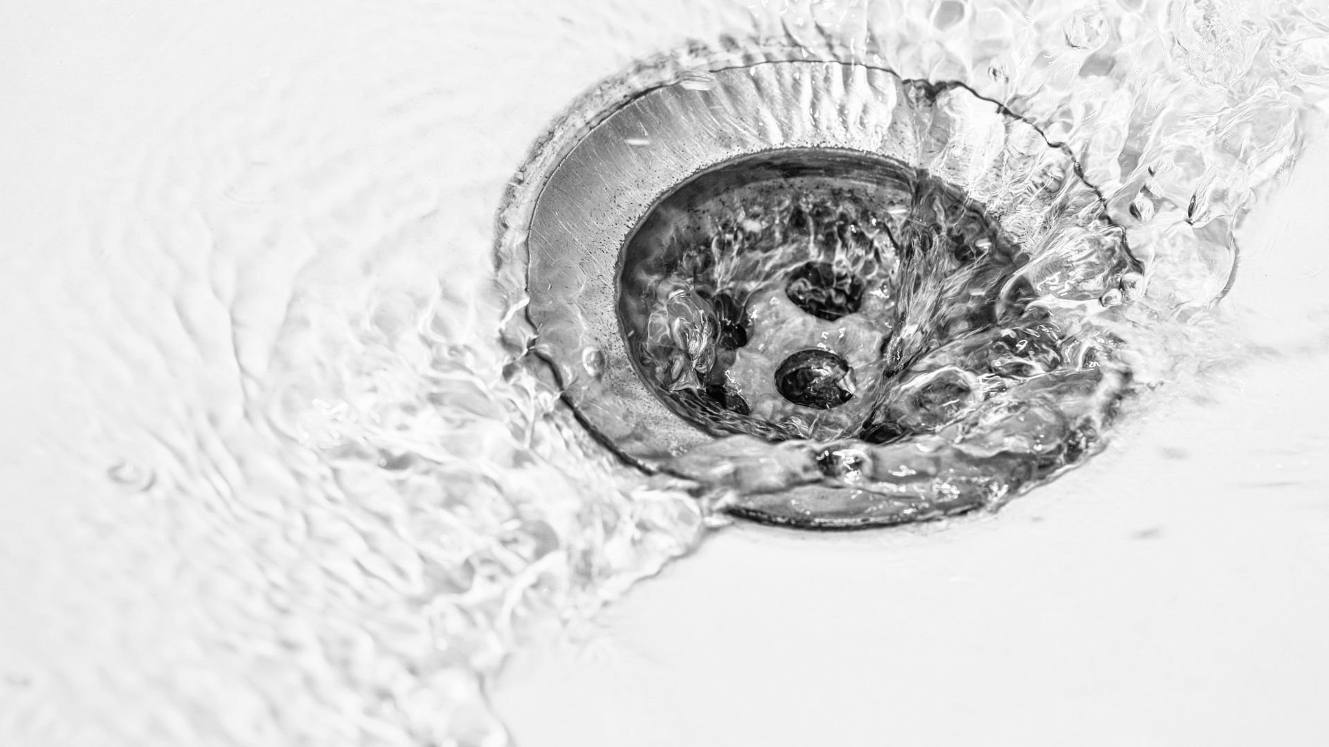 Black and white close-up of water swirling down a drain