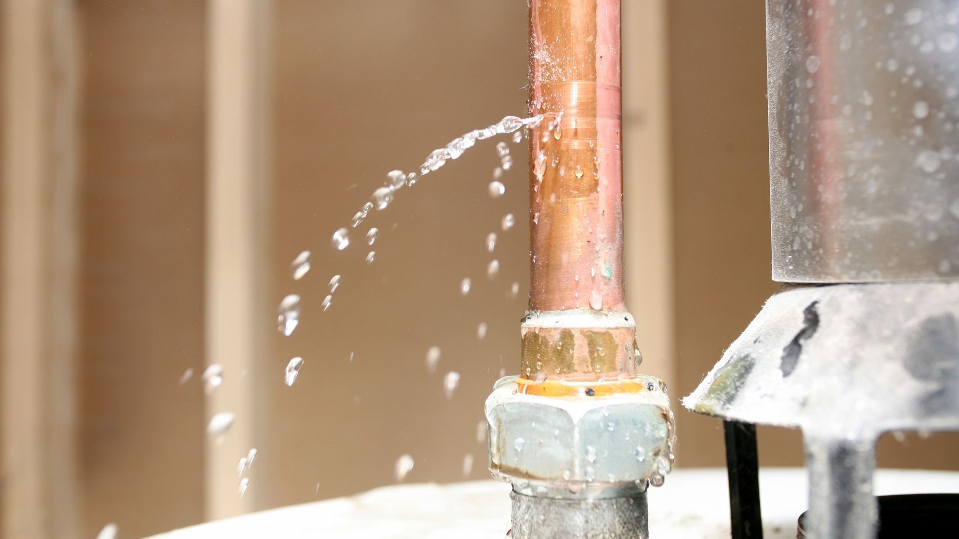 Water leaking from copper pipe connection with water droplets spraying