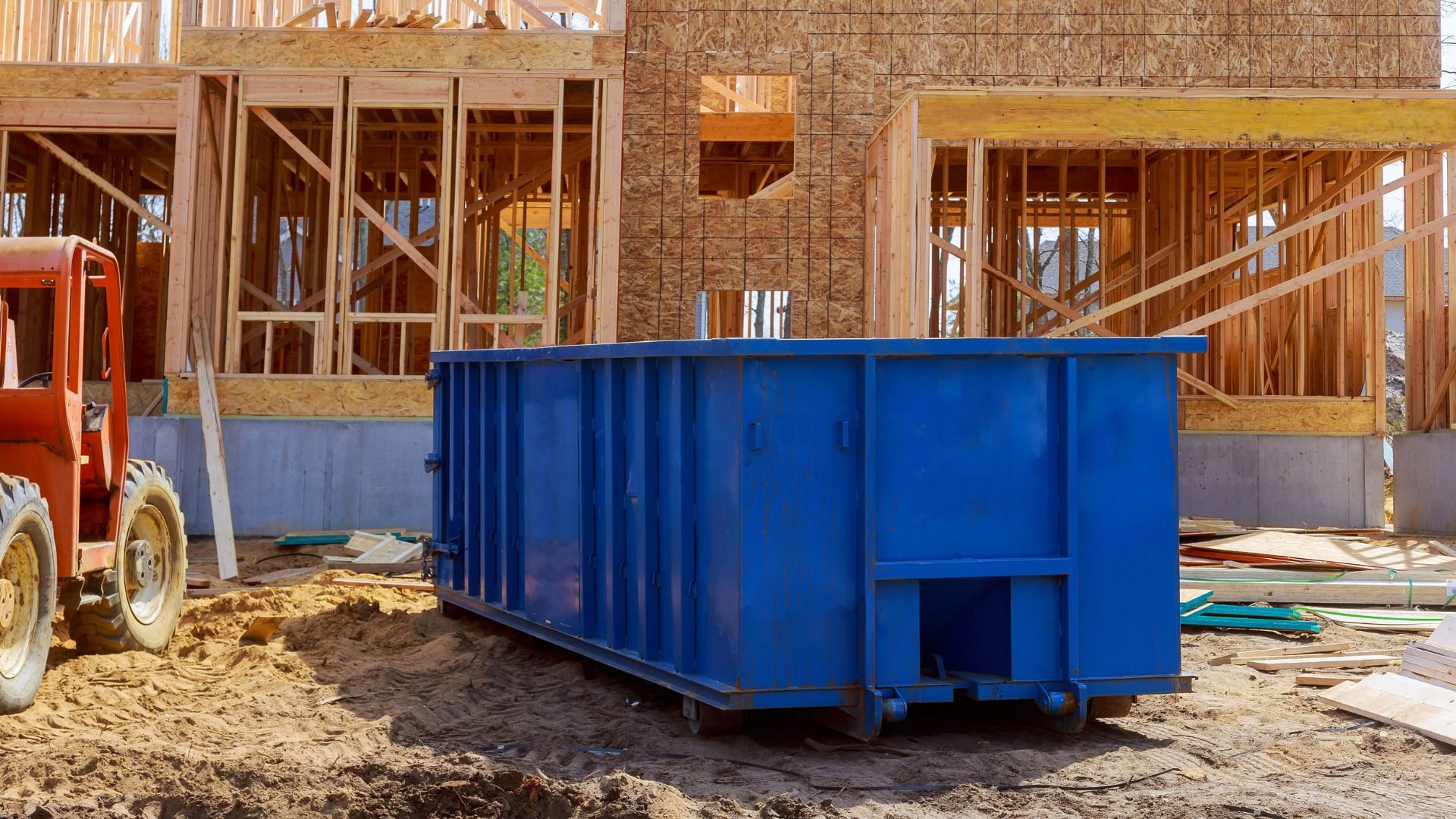 Blue dumpster at residential construction site with wooden framing