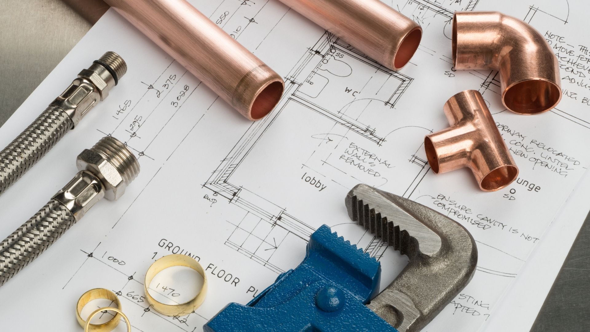 Plumbing tools and copper pipes on architectural blueprint